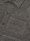 Close-up of a grey marl wool fleece uniform jacket on a plain white backdrop. The shot shows the spread collar, three dark horn-effect buttons on the placket, and a large patch pocket visible on the chest. The brushed, fleecy wool texture is prominent across the fabric.