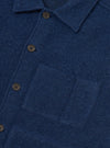 Close-up of an indigo wool fleece uniform jacket on a white studio backdrop. The brushed, textured fleece fabric is shown in detail, with a spread collar, four-hole dark horn-effect buttons on a front placket, and a large patch pocket on the chest.