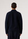 Back view of a male model wearing a navy wool fleece uniform jacket against a light grey studio backdrop. The textured fleece fabric is visible across the back and full-length sleeves. A spread collar is visible at the neckline. The jacket sits at hip length with a ribbed hem. Worn over navy trousers. Shot cropped above the knees.