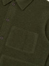 Close-up of an olive wool fleece uniform jacket on a plain white studio backdrop. The shot shows the point collar, button placket with dark four-hole buttons, and a large patch pocket on the chest. The boiled wool texture is clearly visible throughout.
