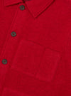 Close-up of a scarlet wool fleece uniform jacket on a plain white studio backdrop. The shot shows a spread collar, a buttoned placket with dark horn-style four-hole buttons, and a large patch pocket on the chest. The brushed wool fleece texture is clearly visible throughout.