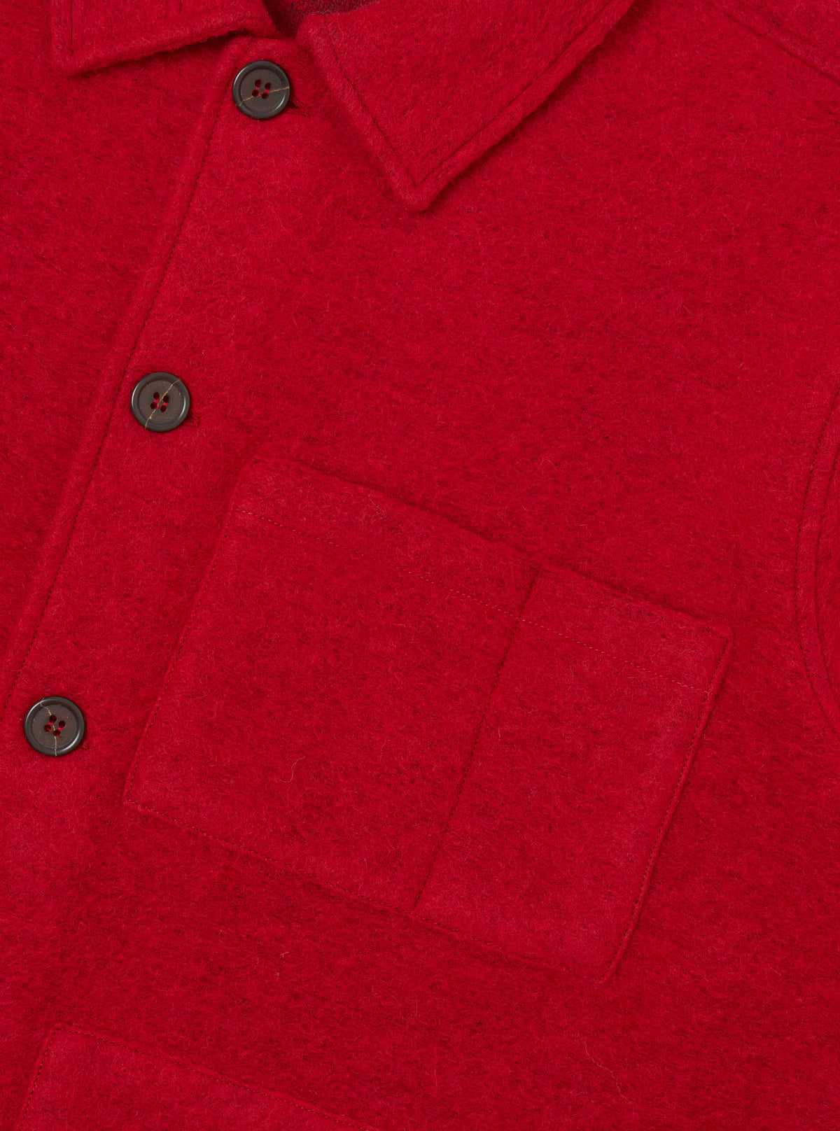 Close-up of a scarlet wool fleece uniform jacket on a plain white studio backdrop. The shot shows a spread collar, a buttoned placket with dark horn-style four-hole buttons, and a large patch pocket on the chest. The brushed wool fleece texture is clearly visible throughout.