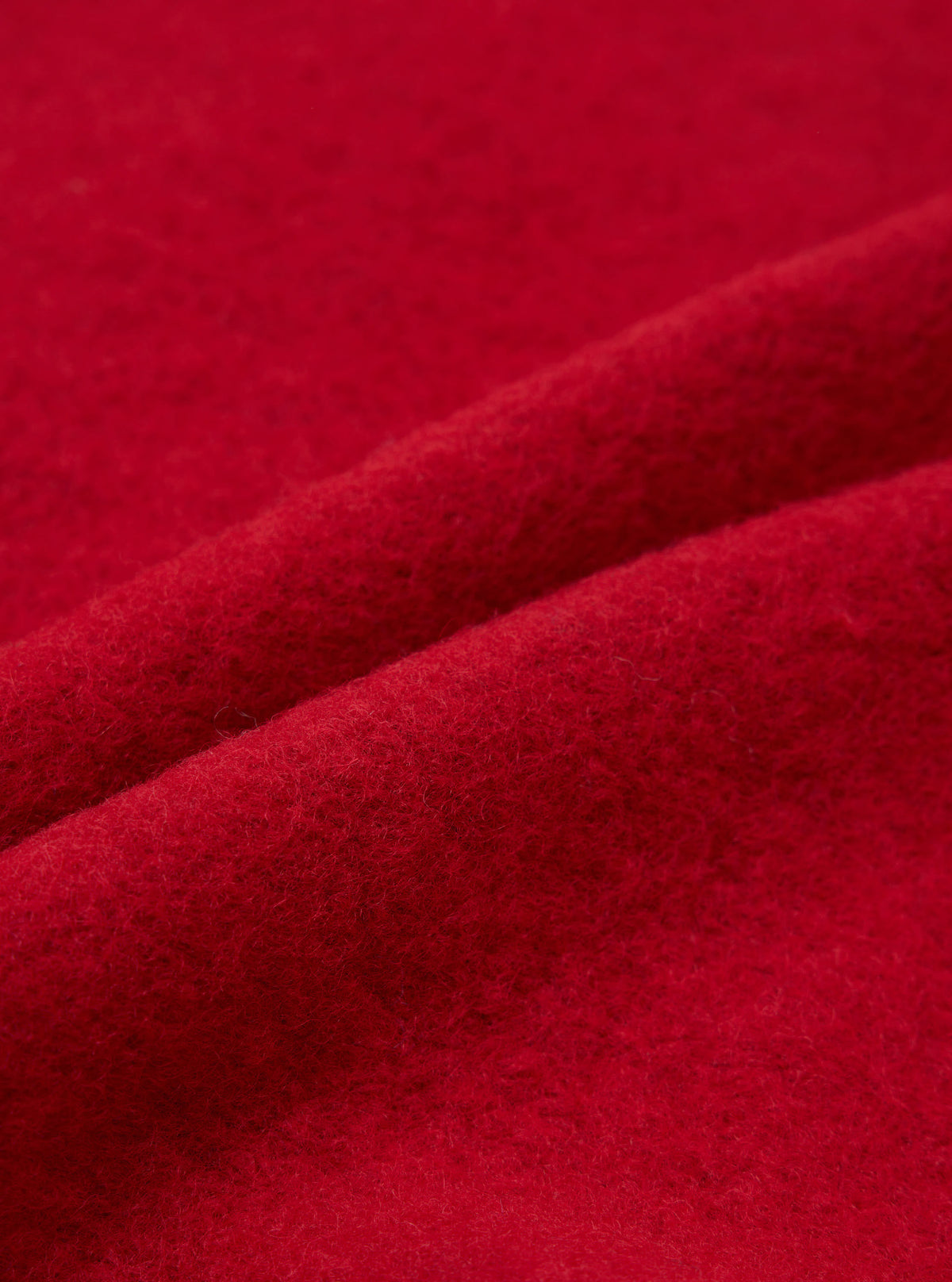 Close-up detail shot of scarlet red boiled wool fleece fabric, showing a soft, dense, lightly felted texture with fine surface fibres. The material is folded to reveal depth and drape. No garment details or construction features are visible. Plain red fabric fills the entire frame.