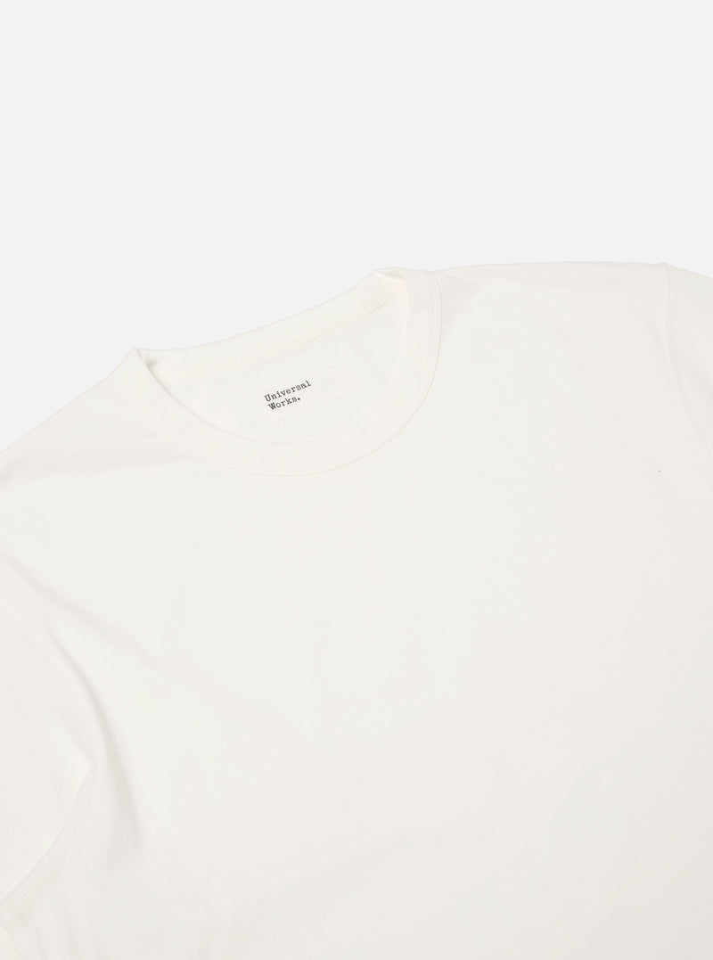 Close-up of the Ecru Single Jersey Core Tee on a white background. The soft, neutral color and smooth fabric are highlighted. The brand label is visible at the neck.