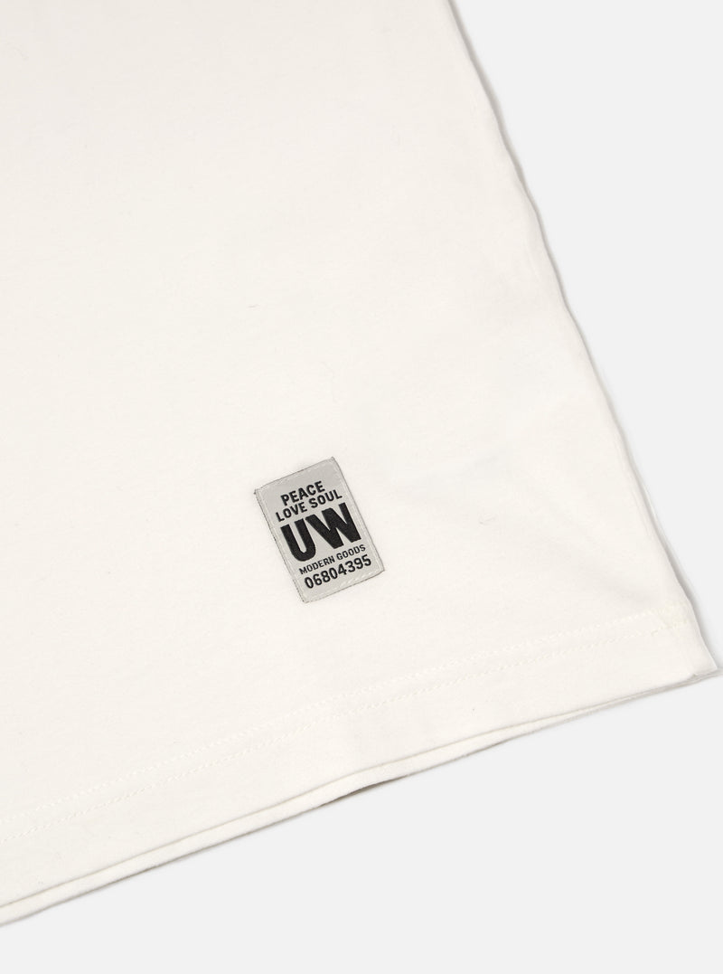 Close-up of the Ecru Single Jersey Core Tee on a white surface, showing the fabric texture and UW label. The tee has a classic, comfortable fit.