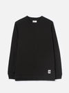 Black long-sleeve jersey T-shirt laid flat on a light grey studio backdrop. Crew neck with a visible Universal Works woven label at the back neck. Single chest patch pocket on the left breast. Ribbed cuffs at the wrists. Small branded UW woven badge at the lower right hem. Plain smooth fabric throughout.