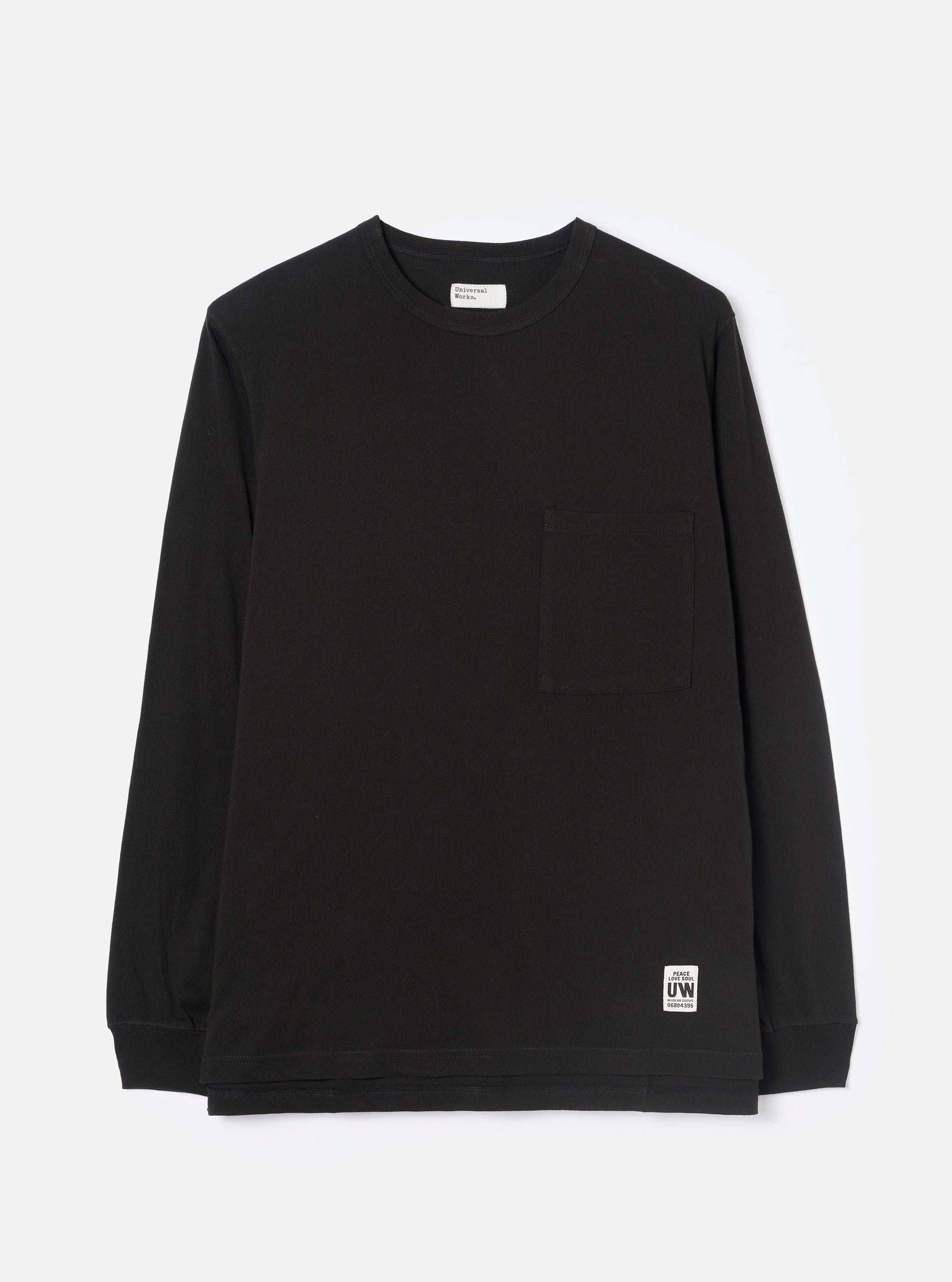 Black long-sleeve jersey T-shirt laid flat on a light grey studio backdrop. Crew neck with a visible Universal Works woven label at the back neck. Single chest patch pocket on the left breast. Ribbed cuffs at the wrists. Small branded UW woven badge at the lower right hem. Plain smooth fabric throughout.