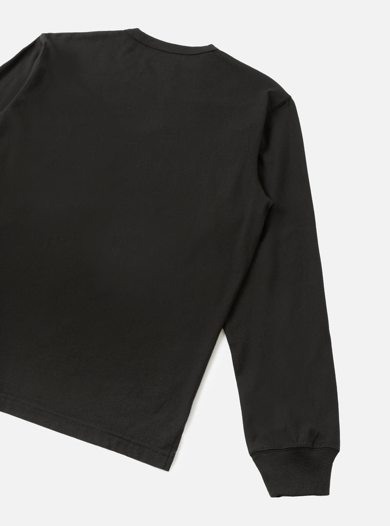 Back detail of a black long-sleeve pocket tee in smooth single jersey cotton. The shot shows the upper back, right shoulder, and full sleeve, cropped at the hem. A ribbed cuff is visible at the wrist. Plain light grey studio backdrop. No model or mannequin present.
