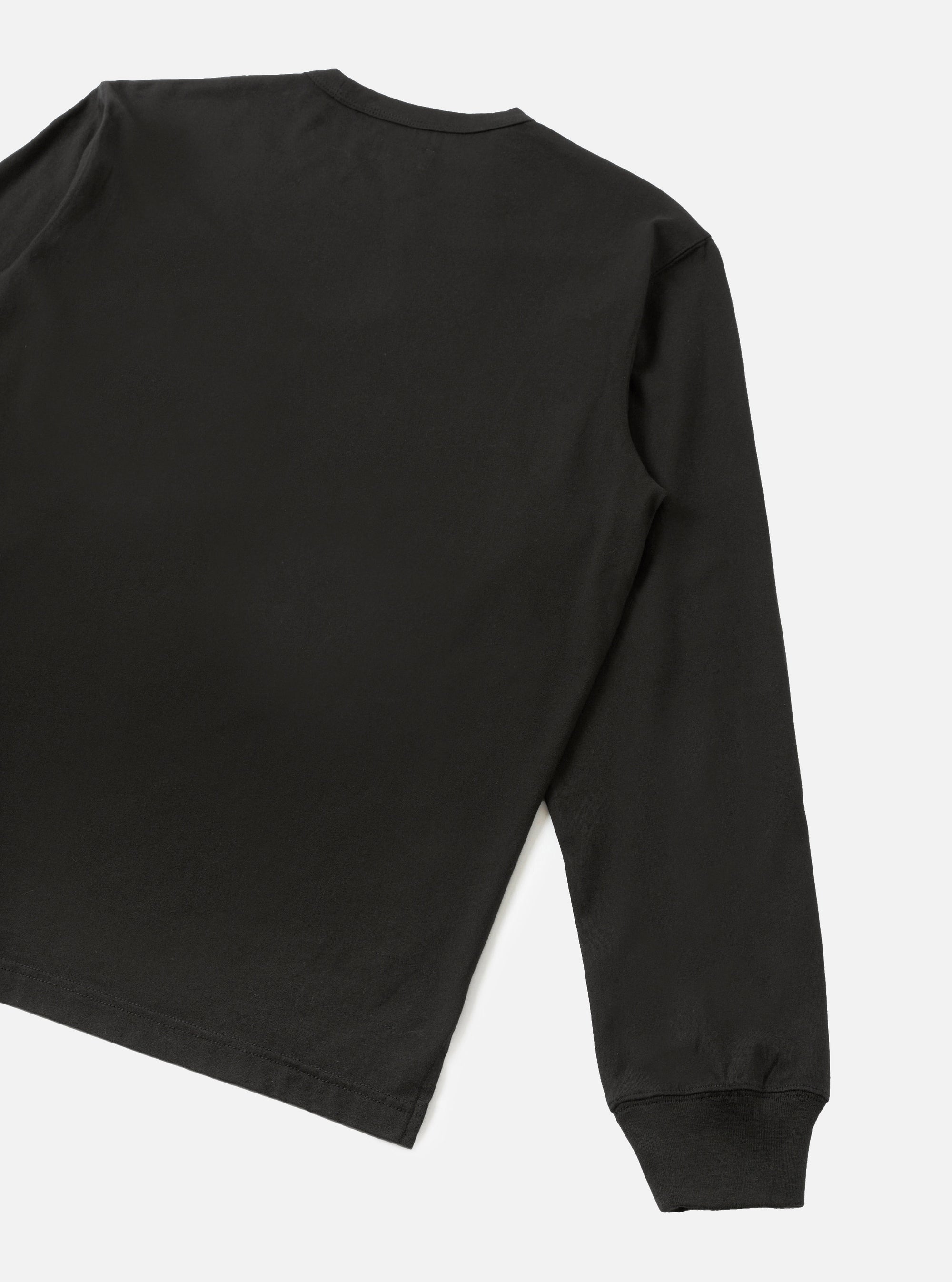 Back detail of a black long-sleeve pocket tee in smooth single jersey cotton. The shot shows the upper back, right shoulder, and full sleeve, cropped at the hem. A ribbed cuff is visible at the wrist. Plain light grey studio backdrop. No model or mannequin present.