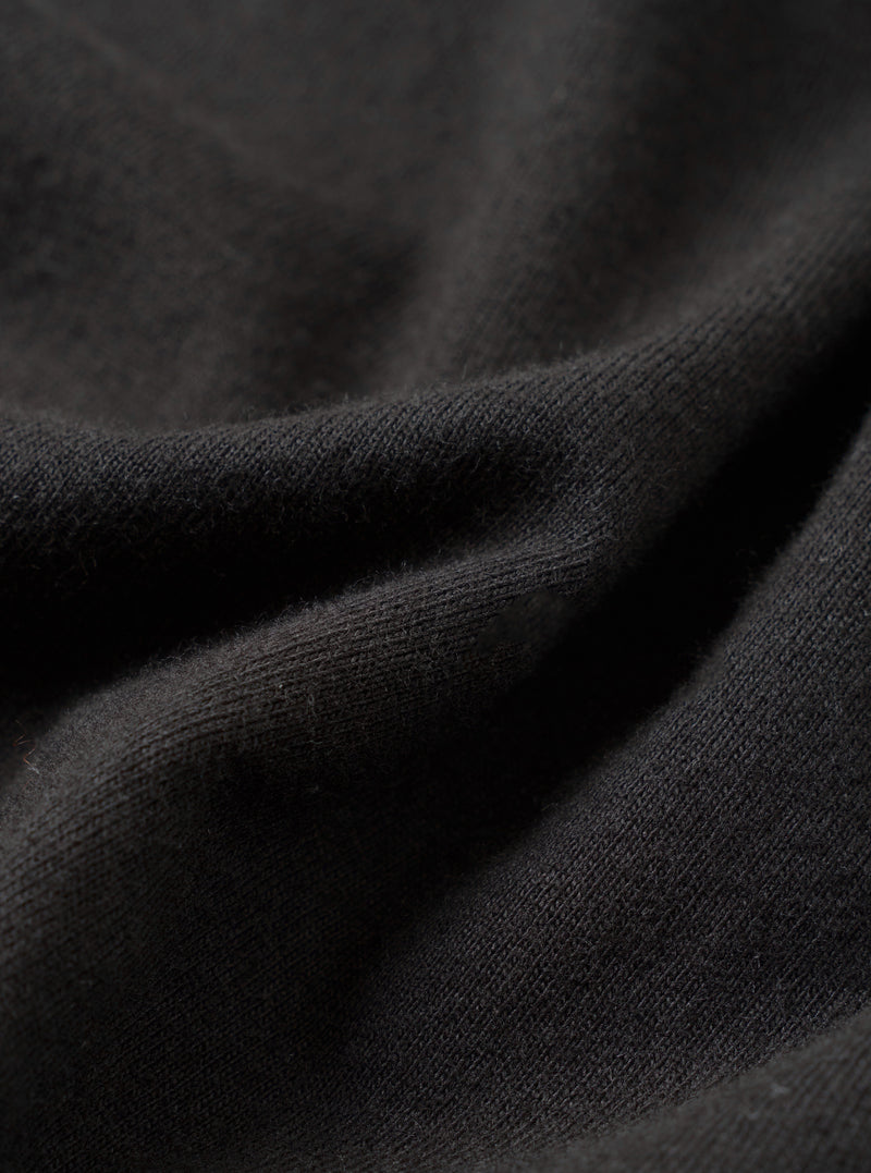 Close-up detail shot of a black single jersey knit fabric, showing soft draping folds with a fine, smooth knit texture visible at the ridges. The surface has a slightly brushed, matte finish. No garment details or background are distinguishable at this macro scale.