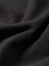 Close-up detail shot of a black single jersey knit fabric, showing soft draping folds with a fine, smooth knit texture visible at the ridges. The surface has a slightly brushed, matte finish. No garment details or background are distinguishable at this macro scale.