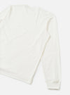 Flat lay of an ecru long-sleeve pocket tee on a light grey seamless backdrop. The shot is cropped to show the back and one full sleeve. The fabric is smooth single jersey cotton with natural drape. A ribbed cuff finishes the sleeve hem.