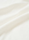 Close-up of ecru single jersey fabric, showing a soft, fine knit texture with natural drape and gentle folds. The off-white tone is even throughout, with a smooth surface and subtle sheen visible across the raised folds of the cloth.