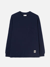 Navy long-sleeve cotton jersey T-shirt laid flat on a light grey seamless backdrop. Features a ribbed crew neck, a single patch chest pocket, and ribbed cuffs. A woven brand label sits at the interior neck and a small printed UW logo tab is sewn at the lower hem. Plain, smooth fabric with no pattern.