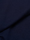 Close-up of navy single jersey fabric showing a fine knit texture with subtle slub variation. A diagonal fold runs across the frame, creating depth and shadow. The plain, solid navy colour is consistent across the textile surface.