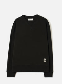 Black crew neck sweatshirt laid flat on a white studio backdrop. Ribbed collar with a V-stitch detail at the chest, ribbed cuffs and hem. Small woven UW brand label at the lower right. Universal Works woven label visible inside the collar. Smooth brushback jersey fabric throughout.