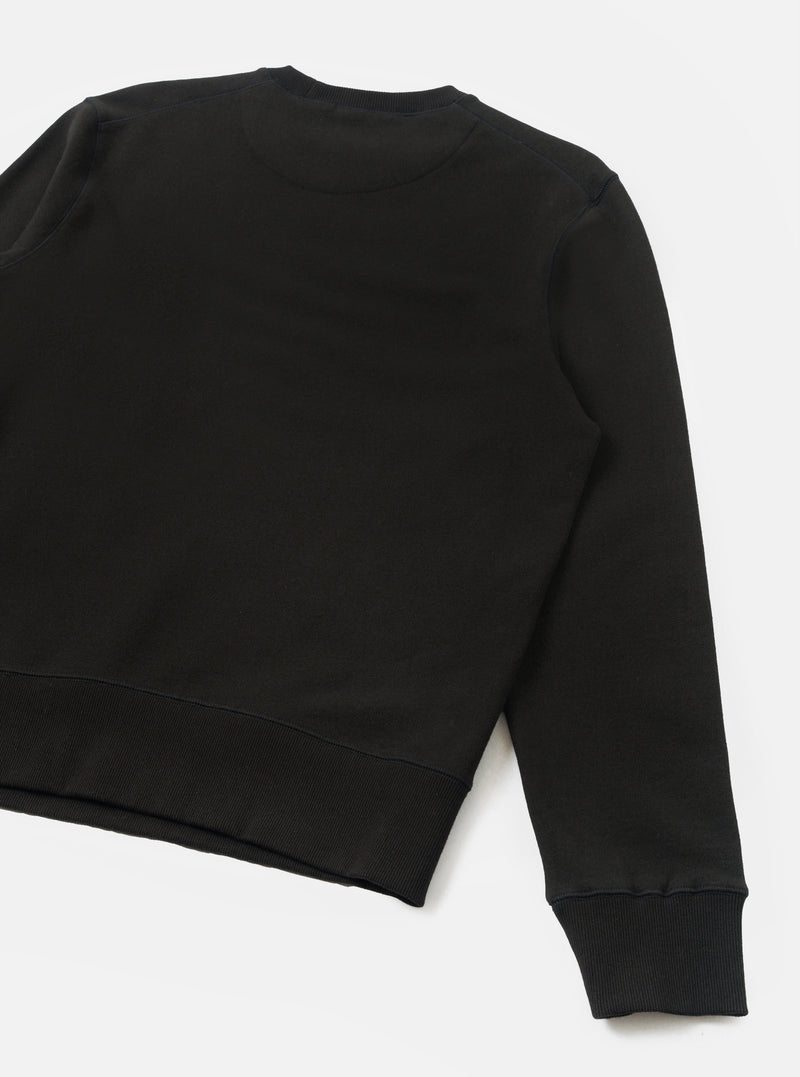 Black brushback core sweatshirt laid flat on a white surface, shot from above at an angle. The crew neck, ribbed hem and ribbed cuff on one long sleeve are visible. The smooth jersey face fabric contrasts with the structured ribbing. No graphics or embellishments are present.