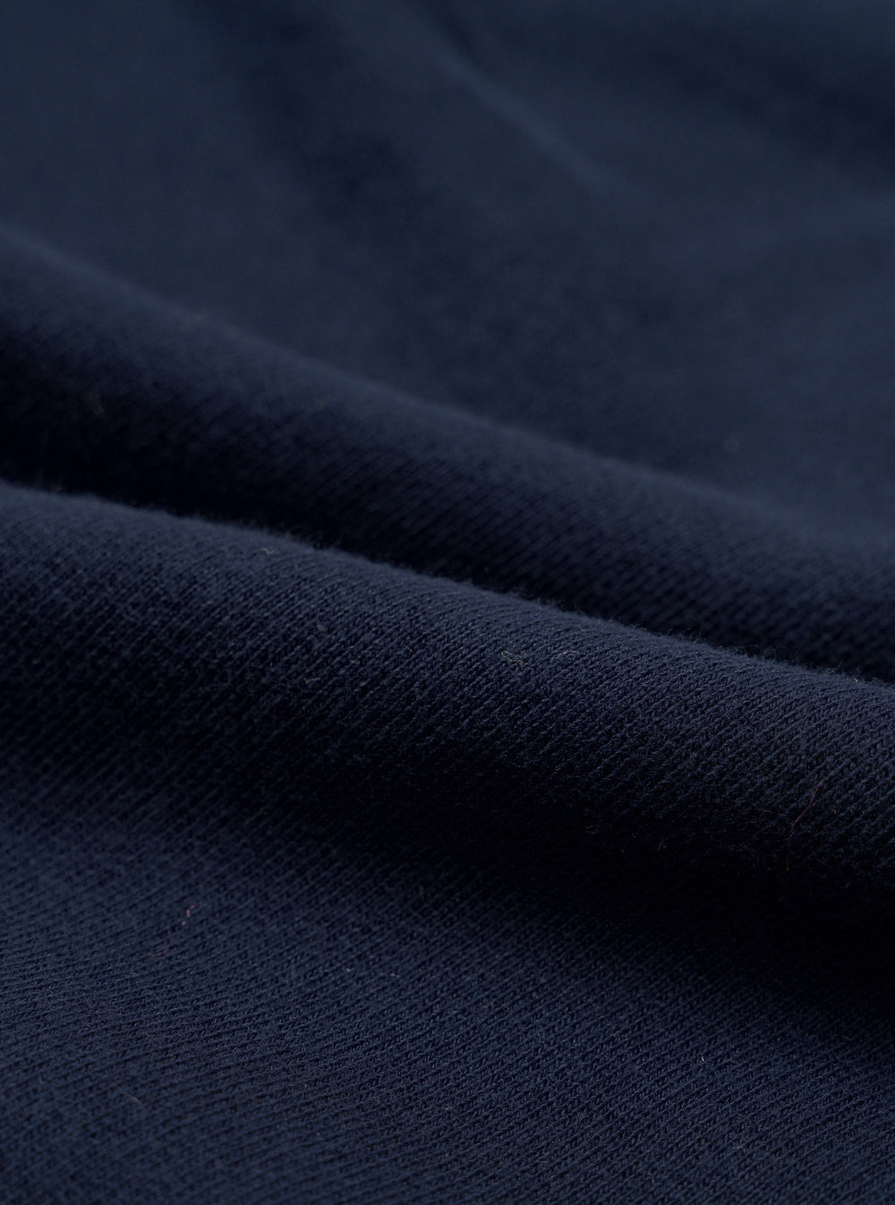 Close-up of navy brushback fleece fabric, showing a soft, dense knit texture with a smooth face and subtle pile. The material is folded to reveal its weight and structure. No garment details or background are visible.