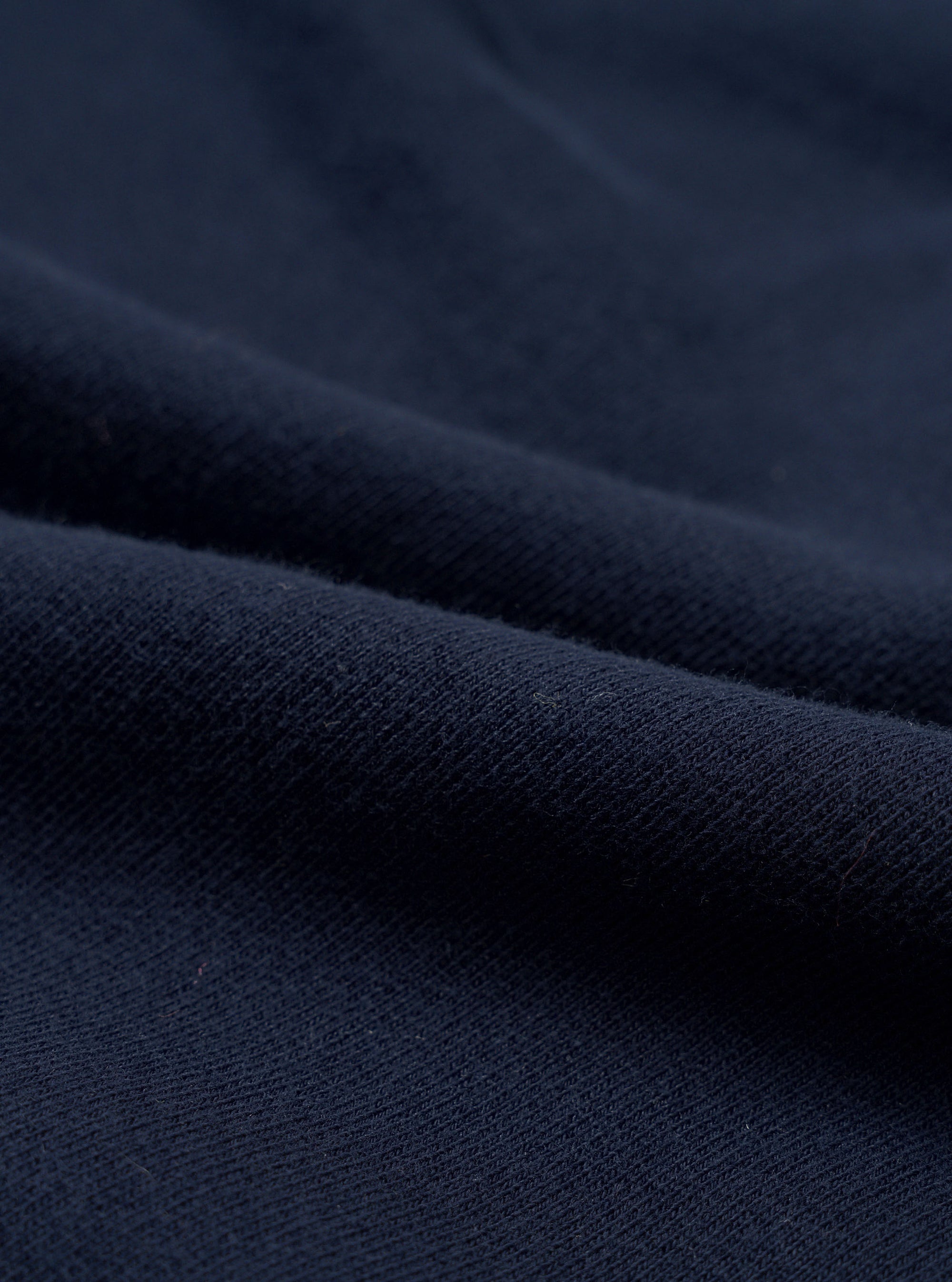 Close-up of navy brushback fleece fabric, showing a soft, dense knit texture with a smooth face and subtle pile. The material is folded to reveal its weight and structure. No garment details or background are visible.