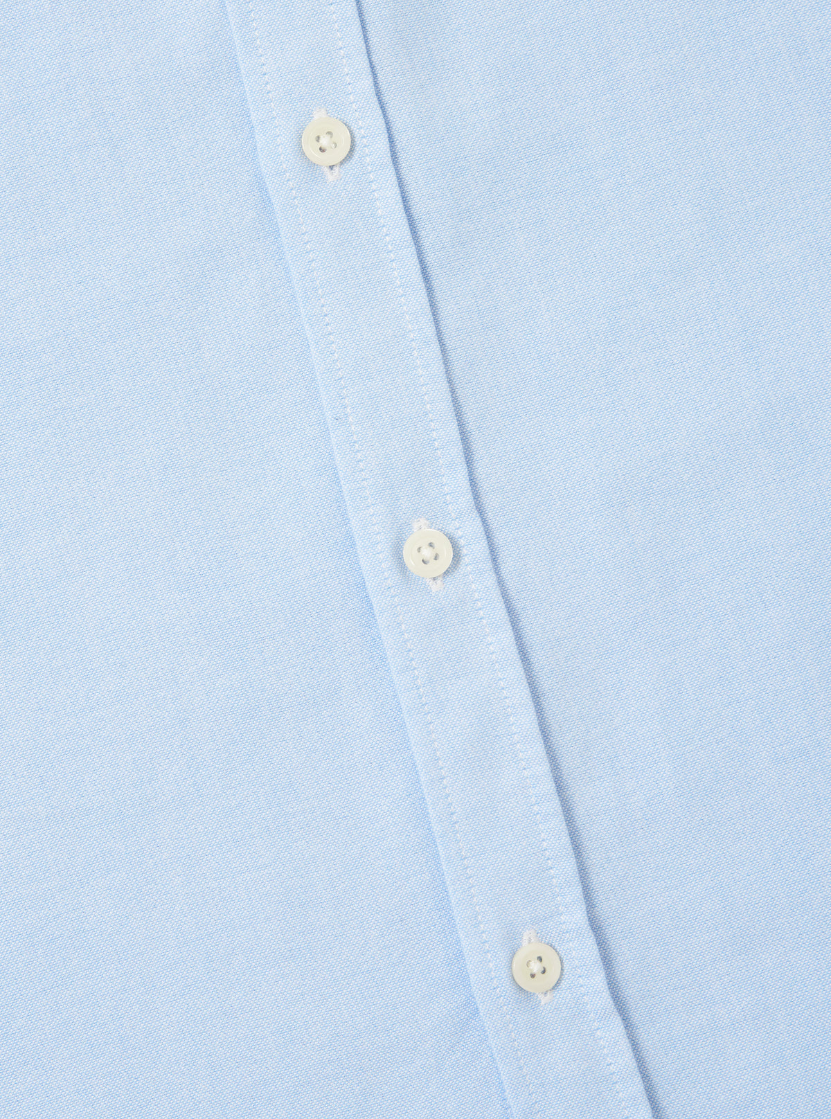 Close-up of the Sky Blue Oxford Daybrook Shirt showing the light blue oxford cloth and button placket with white buttons. Shot on a white surface.