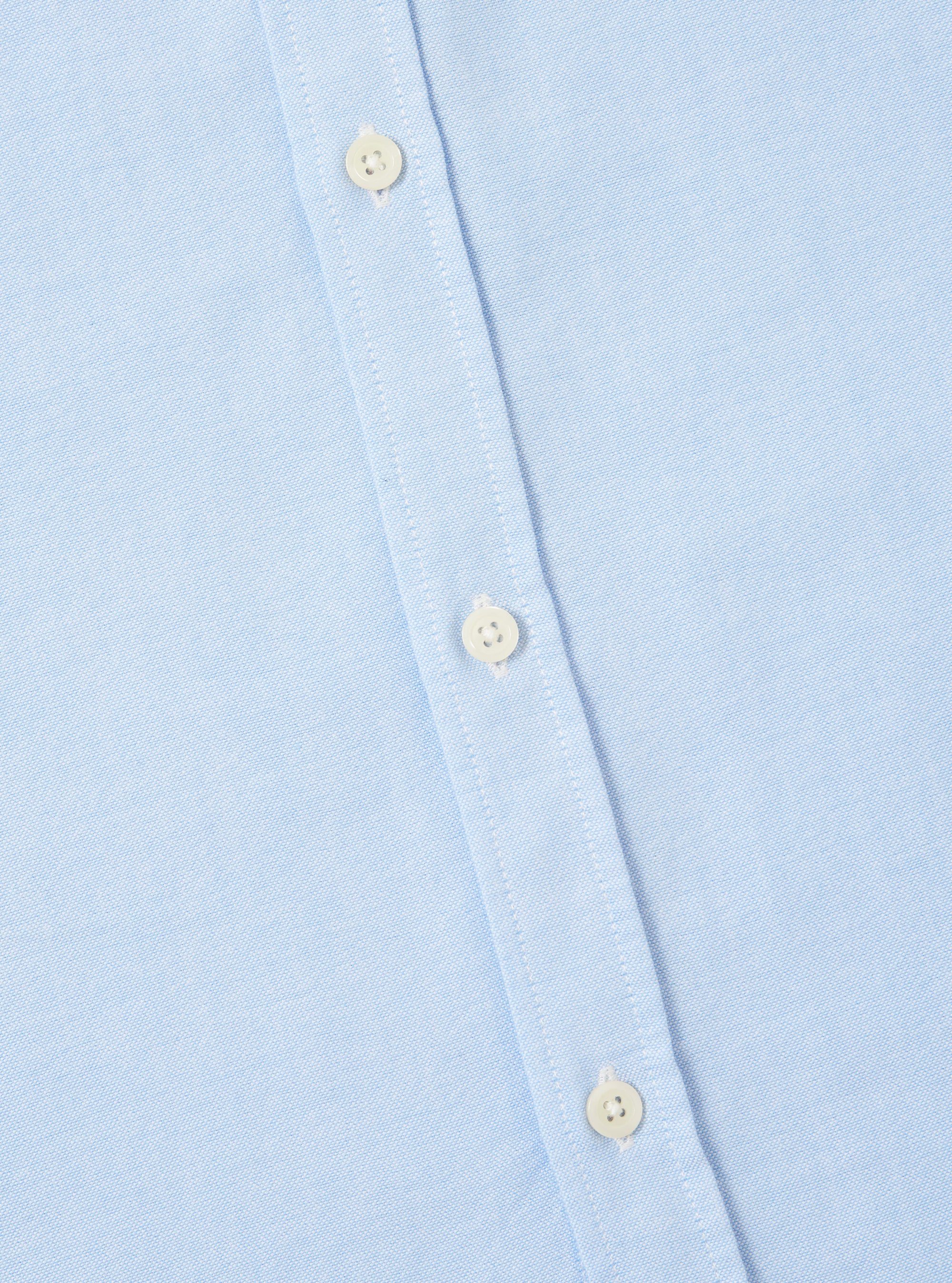 Close-up of the Sky Blue Oxford Daybrook Shirt showing the light blue oxford cloth and button placket with white buttons. Shot on a white surface.