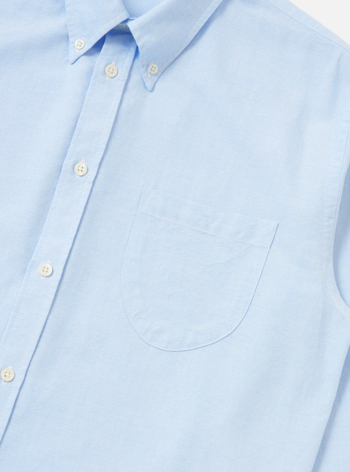 Close-up of the Sky Blue Oxford Daybrook Shirt on a flat white surface. The light blue cotton shirt features a button-down collar and a chest pocket.