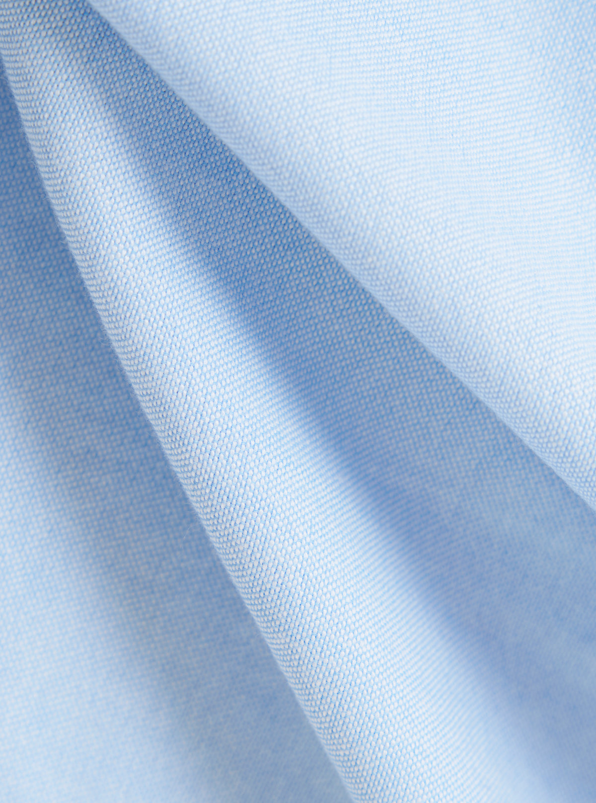 Close-up of the Sky Blue Oxford Daybrook Shirt fabric. The light blue woven material is softly draped, showcasing the texture and color of the shirt.