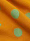 Close-up of the Mustard Bold Dot Print Rayon Scout Scarf, showing the mustard yellow fabric with bold green polka dots. The rayon material has a soft, flowing drape.