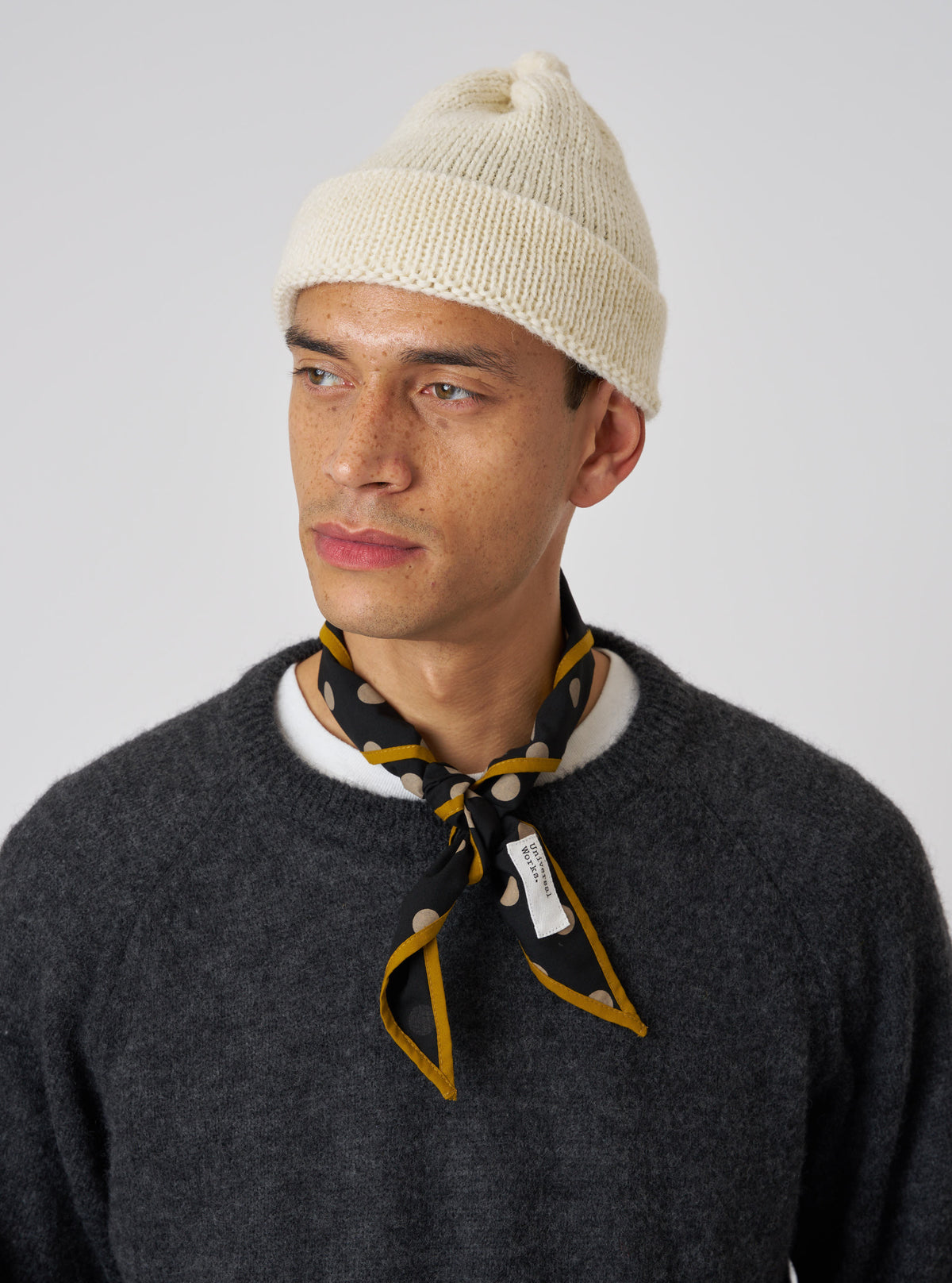 A model wears a Black Bold Dot Print Rayon Scout Scarf tied around his neck. The scarf features gold trim and is styled with a cream beanie and gray sweater against a white background.