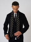 A model in a suit wears a Black Bold Dot Print Rayon Evening Scarf. The scarf has tan dots and is rayon. The background is a plain studio backdrop.