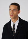 A model wears a Black Bold Dot Print Rayon Tie with a white shirt and black corduroy jacket against a white background. The tie features large tan polka dots.