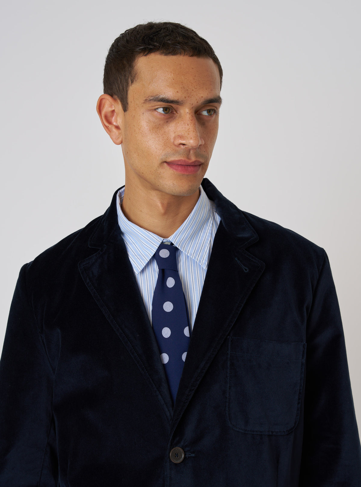A model wears a Navy Bold Dot Print Rayon Tie with a blue striped shirt and navy velvet blazer against a white background.