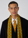 A model wears a Mustard Bold Dot Print Rayon Evening Scarf. The scarf is mustard with green dots. The background is a plain white wall.
