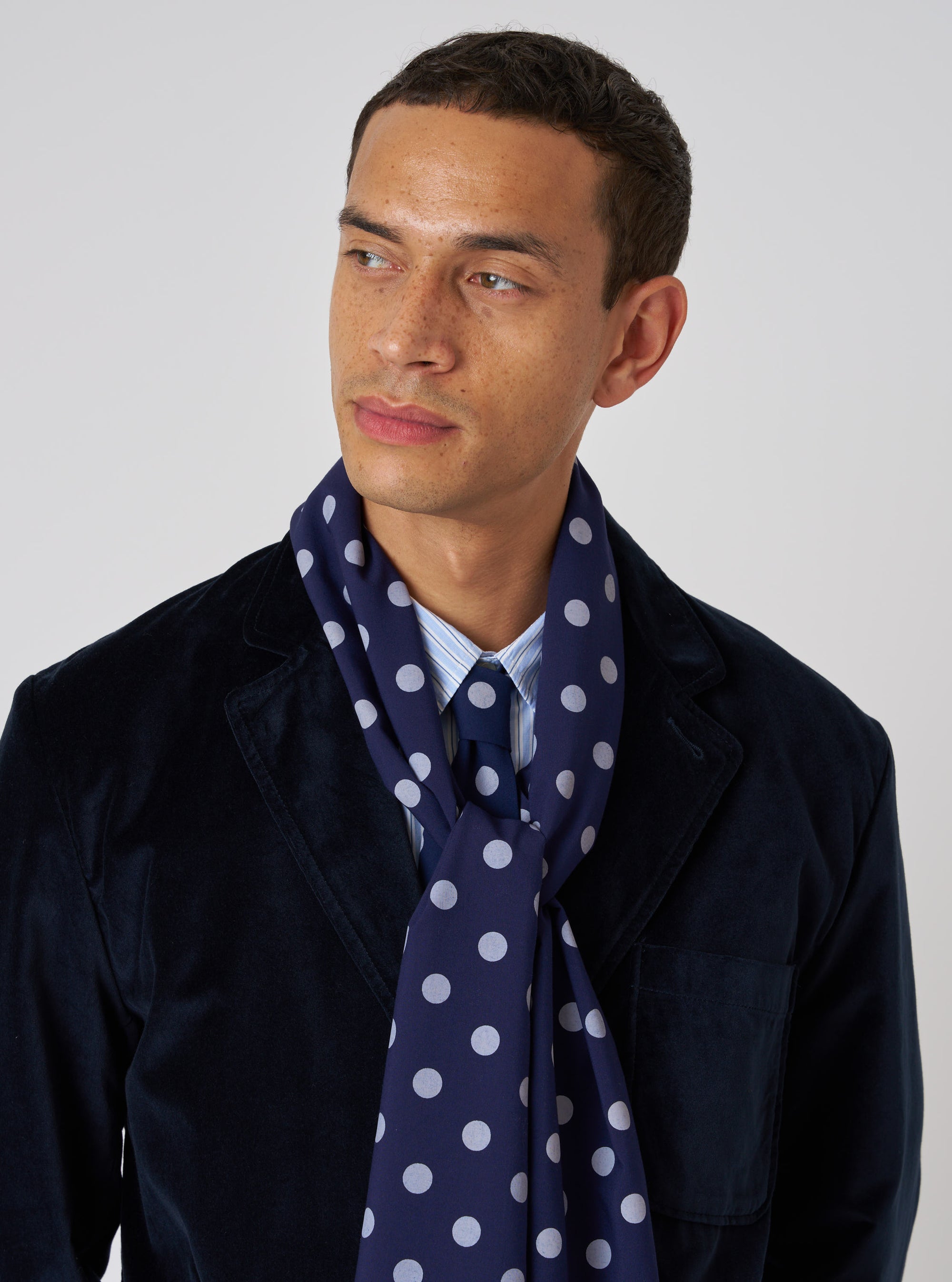A model wears a Navy Bold Dot Print Rayon Evening Scarf with a navy jacket, light blue shirt and tie against a white background. The scarf is draped around his neck.