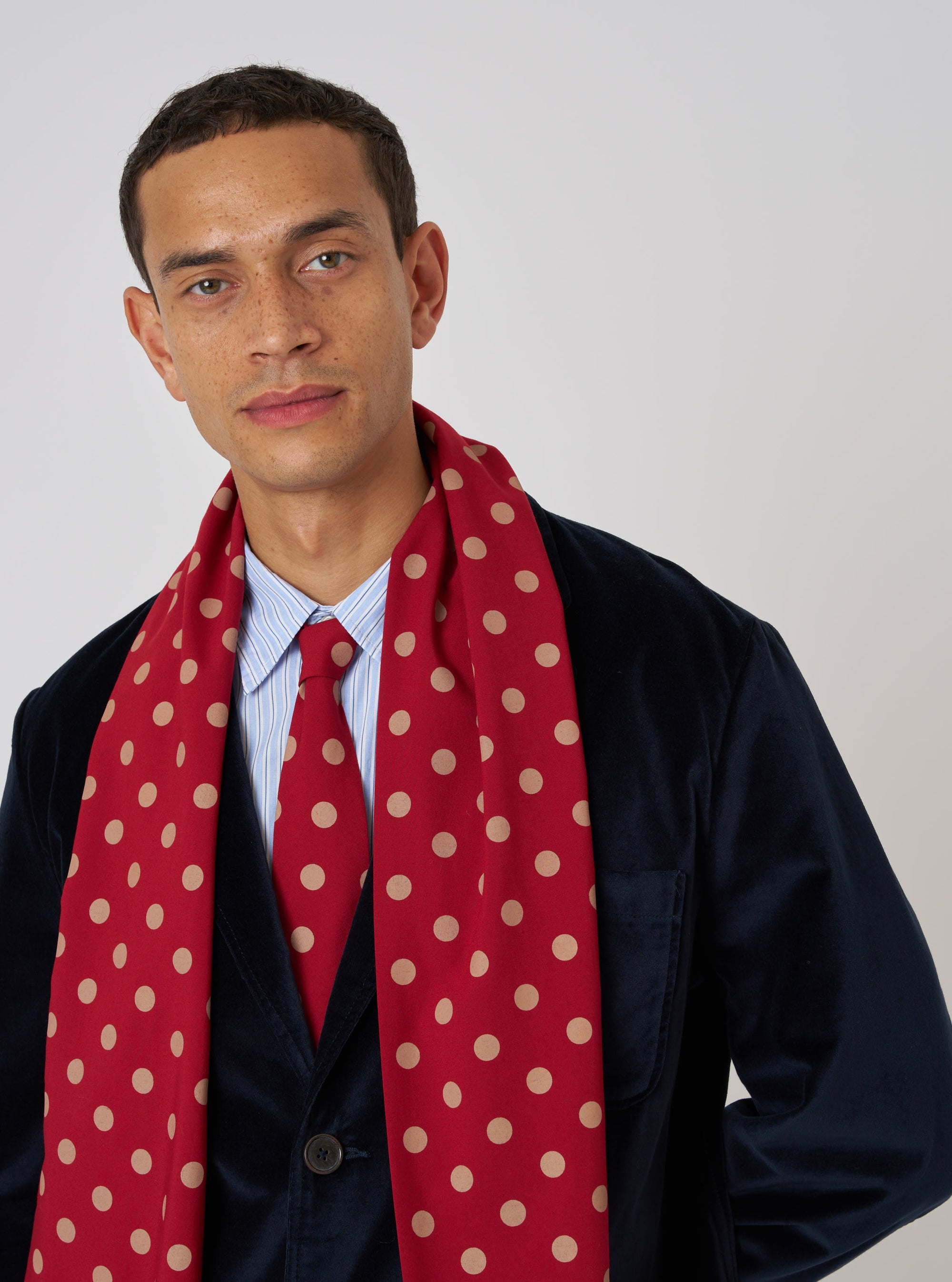 A model wears a Red Bold Dot Print Rayon Evening Scarf with a navy jacket. The scarf is draped around his neck. The background is a plain white.