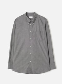 Grey chambray Daybrook shirt by Universal Works, flat lay on a light grey seamless backdrop. Button-down collar with buttoned collar points, full button placket with white buttons, single chest patch pocket, and long sleeves with buttoned cuffs. Fine woven texture visible throughout. Curved hem. Universal Works woven label at neck.