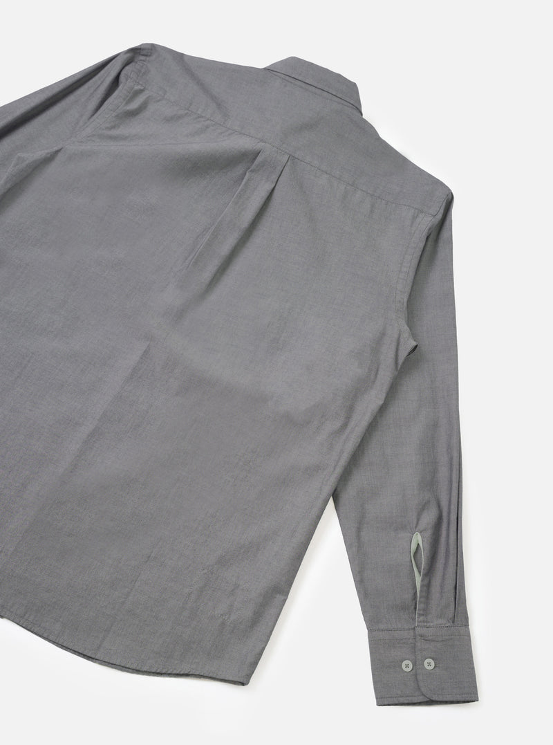 Flat lay of the Black Prince chambray Daybrook shirt on a white studio backdrop, showing the back and one sleeve. The fine-weave grey chambray fabric has a subtle texture. A back yoke seam runs across the shoulders. The cuff is buttoned with two small grey buttons and features a placket opening.