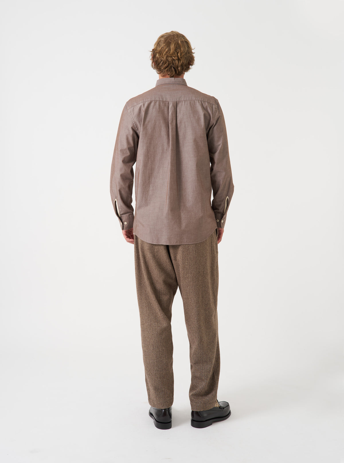 Back view of a male model wearing the Brown Prince Chambray Daybrook Shirt against a plain light grey backdrop. The long-sleeve cotton shirt has a classic button-down fit with a smooth back yoke.