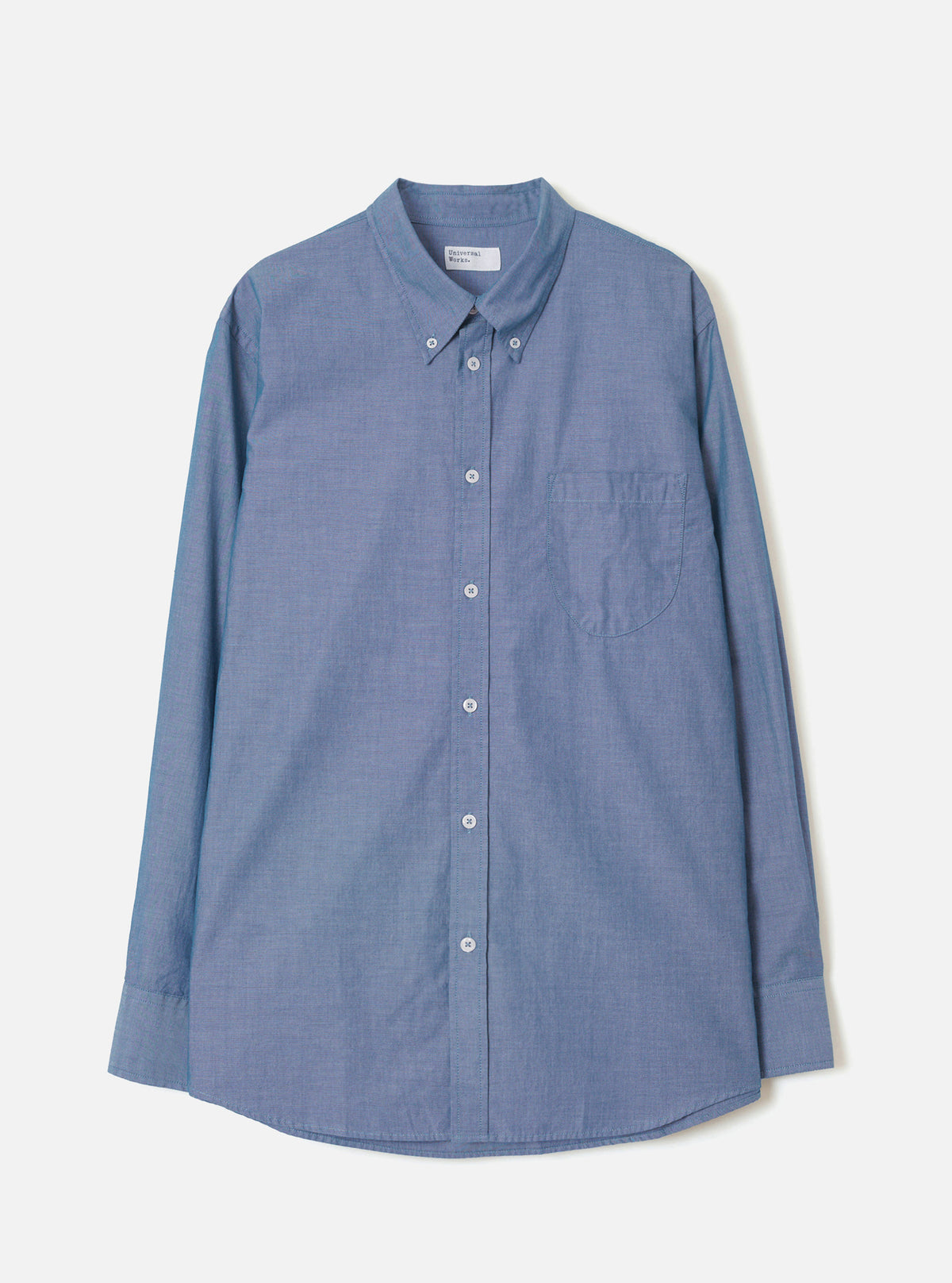 Front view of the Indigo Prince Chambray Daybrook Shirt laid flat on a light grey studio backdrop. Features a spread collar, full button placket with white buttons, a single chest patch pocket, and long sleeves with buttoned cuffs.
