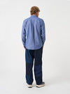 Back view of a male model wearing the Indigo Prince Chambray Daybrook Shirt against a plain light grey studio backdrop. The back panel and long sleeves of the indigo blue chambray shirt are prominently shown.