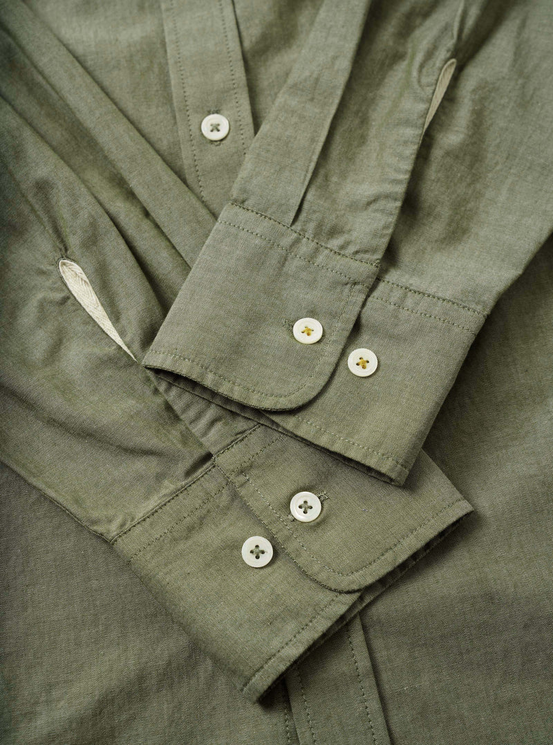 Close-up flat-lay detail of the olive chambray Daybrook shirt, showing two barrel cuffs each fastened with two white four-hole buttons with gold stitching. The placket is visible at the top with a single button. Fine topstitching runs along the cuff edges. The woven chambray fabric has a subtle two-tone texture.