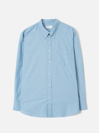 Sky blue chambray long-sleeve shirt laid flat on a light grey seamless backdrop. Button-down collar with a woven Universal Works label at the neck. Centre front button placket with white buttons. Single patch chest pocket on the left. Rounded shirt tail hem and plain cuffs.