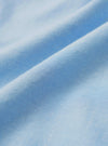 Close-up detail shot of the sky blue chambray fabric used in the Daybrook shirt. The tightly woven oxford-style weave is clearly visible, showing a fine two-tone texture with light and mid-blue threads. The fabric is softly draped, catching light across a diagonal fold.