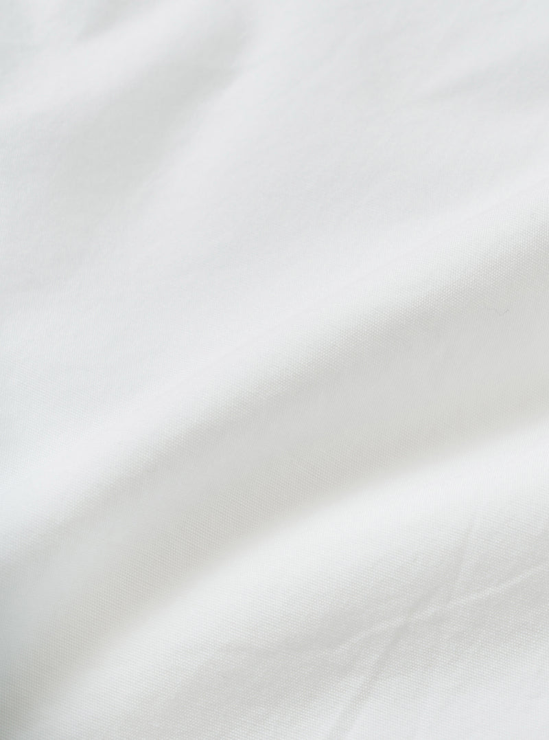 Close-up of the white chambray fabric used in the Daybrook shirt, showing a fine woven texture with a subtle grid-like weave structure. Soft natural folds run diagonally across the frame, highlighting the fabric's lightweight drape and clean white tone. No garment details or model visible.