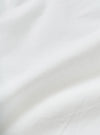 Close-up of the white chambray fabric used in the Daybrook shirt, showing a fine woven texture with a subtle grid-like weave structure. Soft natural folds run diagonally across the frame, highlighting the fabric's lightweight drape and clean white tone. No garment details or model visible.