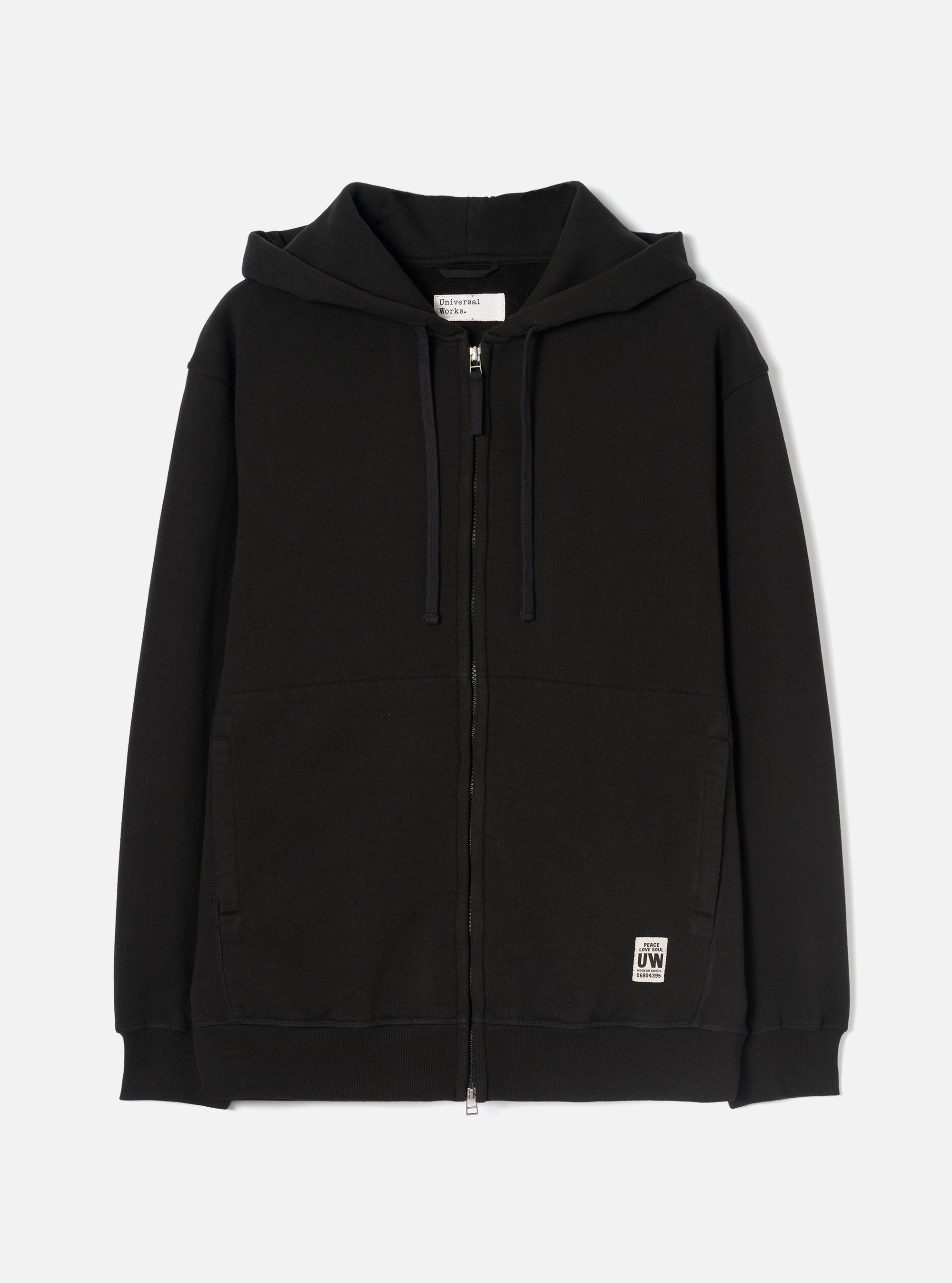 Black zip-through hoodie in brushback sweat fabric, laid flat on a white studio backdrop. Features a jersey-lined hood with navy drawcords, a full-length metal zip, two large patch pockets, and ribbed cuffs and hem. A small woven UW brand label sits at the lower right front.