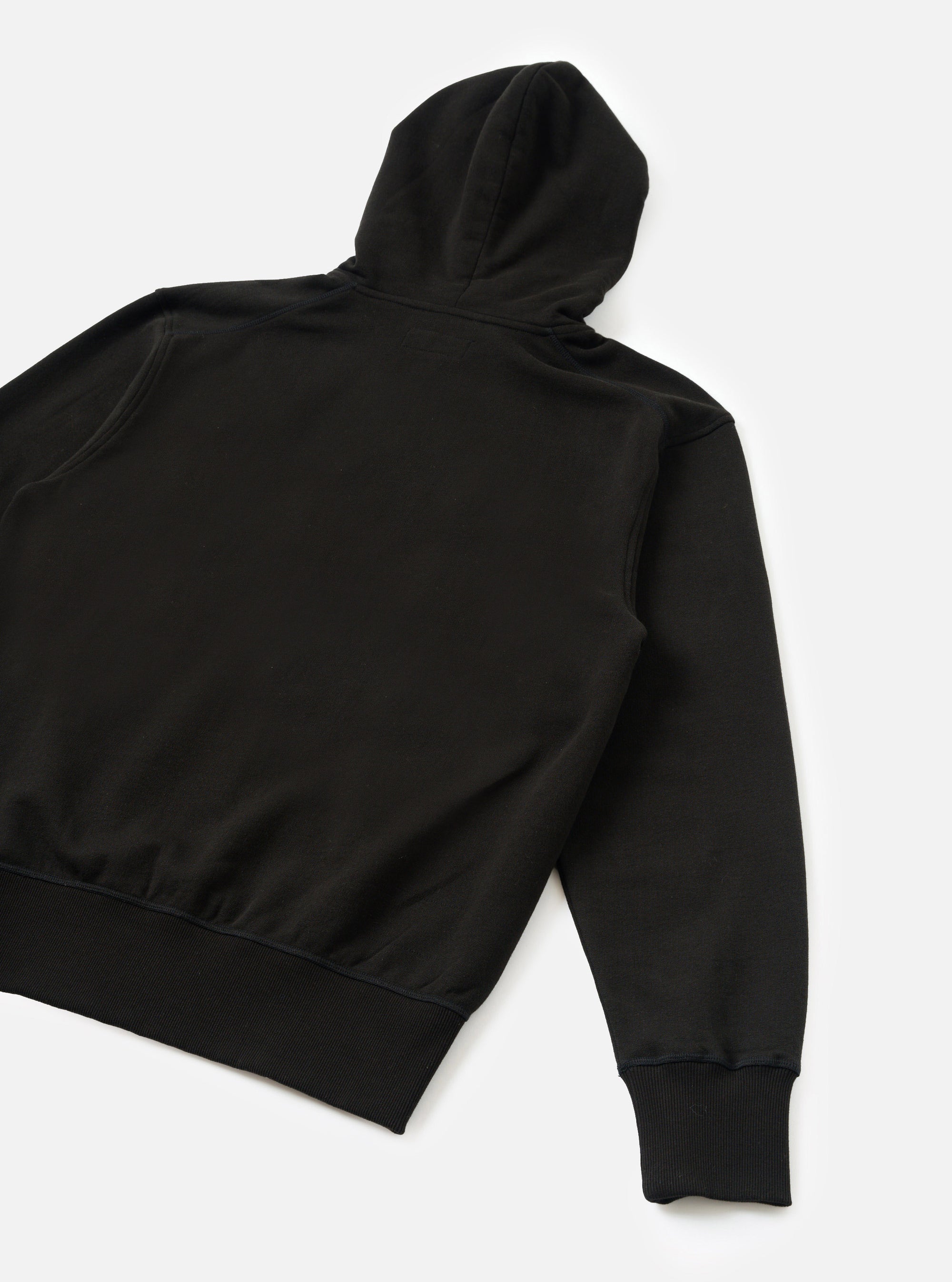 Black brush back hoodie laid flat on a white surface, shot from the back. The smooth jersey back panel, structured hood with a centre seam, one visible long sleeve, ribbed cuff and a wide ribbed hem band are all clearly visible.