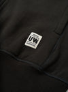 Close-up detail of a black brushback sweat core hoody, showing a woven brand label reading "Peace Love Soul UW Modern Goods 06804395" stitched onto the chest. Ribbed cuff trim is visible at the lower left. The jersey fabric texture is clearly visible against a dark studio backdrop.