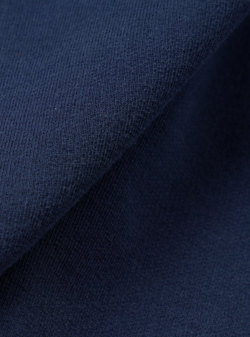 Close-up of the navy brushed-back sweatshirt fabric, showing a soft knit texture with a fine loop structure on the face. The material is folded to reveal depth and drape. No garment details or background are visible.