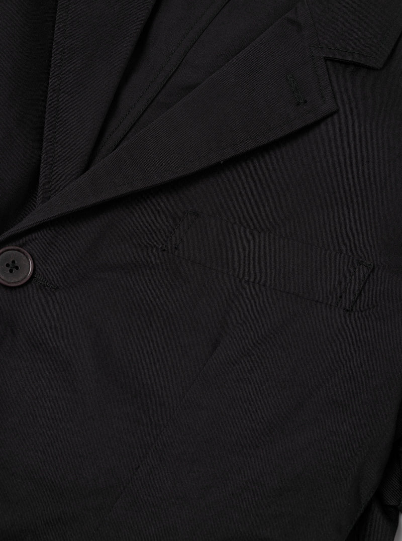 Close-up detail shot of the Black Twill London Jacket laid flat on a plain light background, showing the fine twill fabric texture, button closure detail, interior lining, and welt pocket stitching.